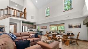 A spacious living area with a high ceiling, a dining table set for six, and a kitchen in the background. - Lakesides Retreat With Amenities (Hollister)