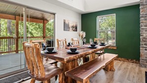 A dining area with a wooden table, chairs, and benches, large windows, and a view of greenery. - Lakesides Retreat With Amenities (Hollister)