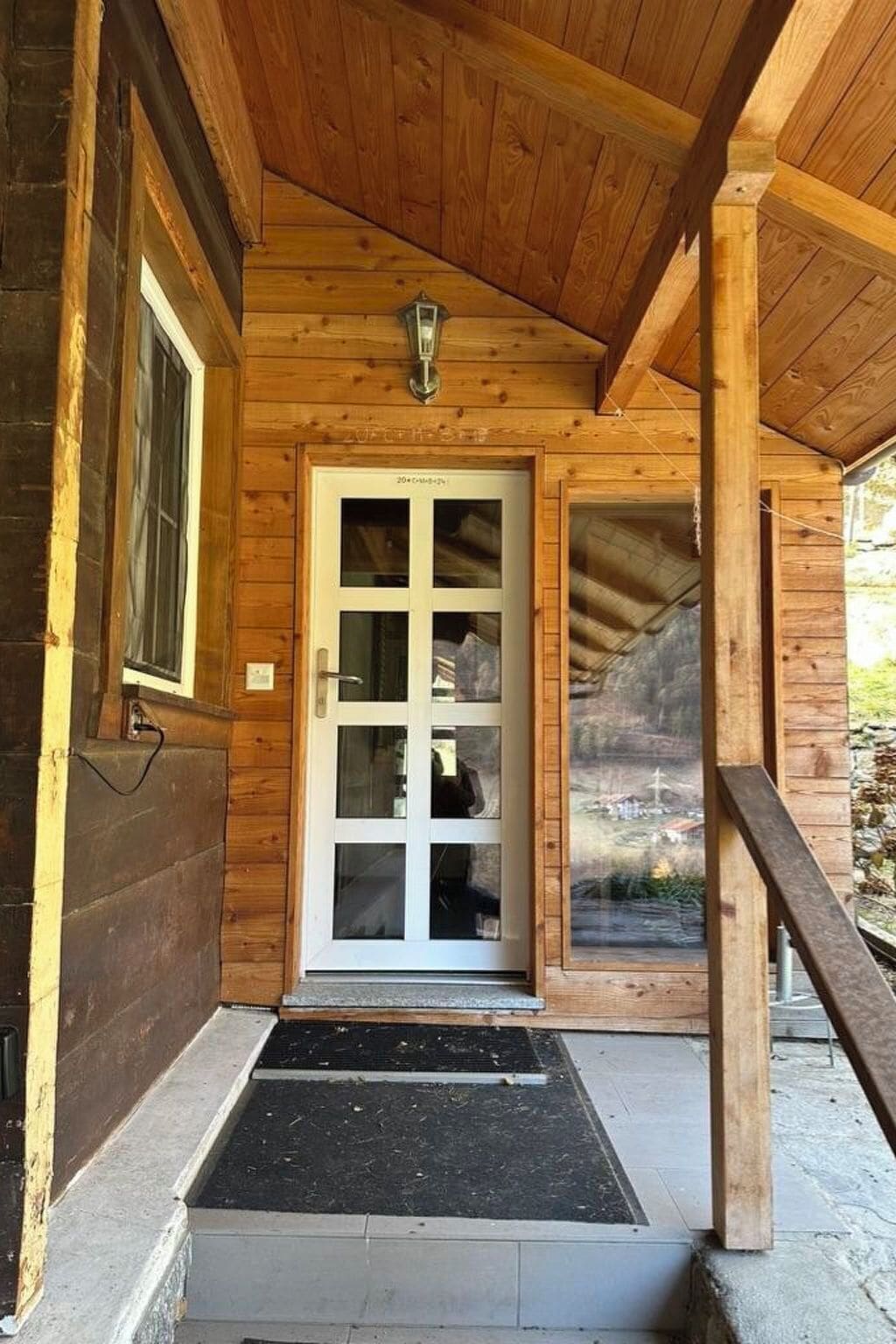 A wooden cabin with a porch, a door with glass panels, and a small window.