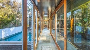 A corridor with glass doors leading to a pool area, surrounded by wooden structures and greenery. - East Lane (Bega Valley)