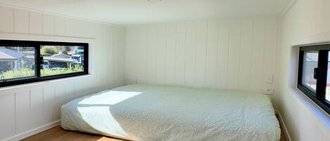 Une pièce avec un plafond en pente, un plancher en bois, un lit recouvert d’une couvre-lit à motifs et deux fenêtres donnant sur l’extérieur.