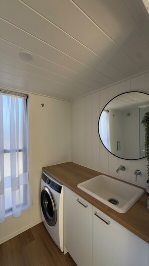 A compact kitchen with a washing machine, a sink, and a mirror. - Cozy tiny home near Cradle Mountain, Burnie & Guide Falls. (Ridgley)
