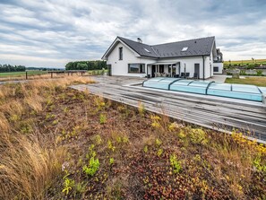 Ein modernes Haus mit Satteldach, einer überdachten Terrasse und einem Garten mit Wildblumen.