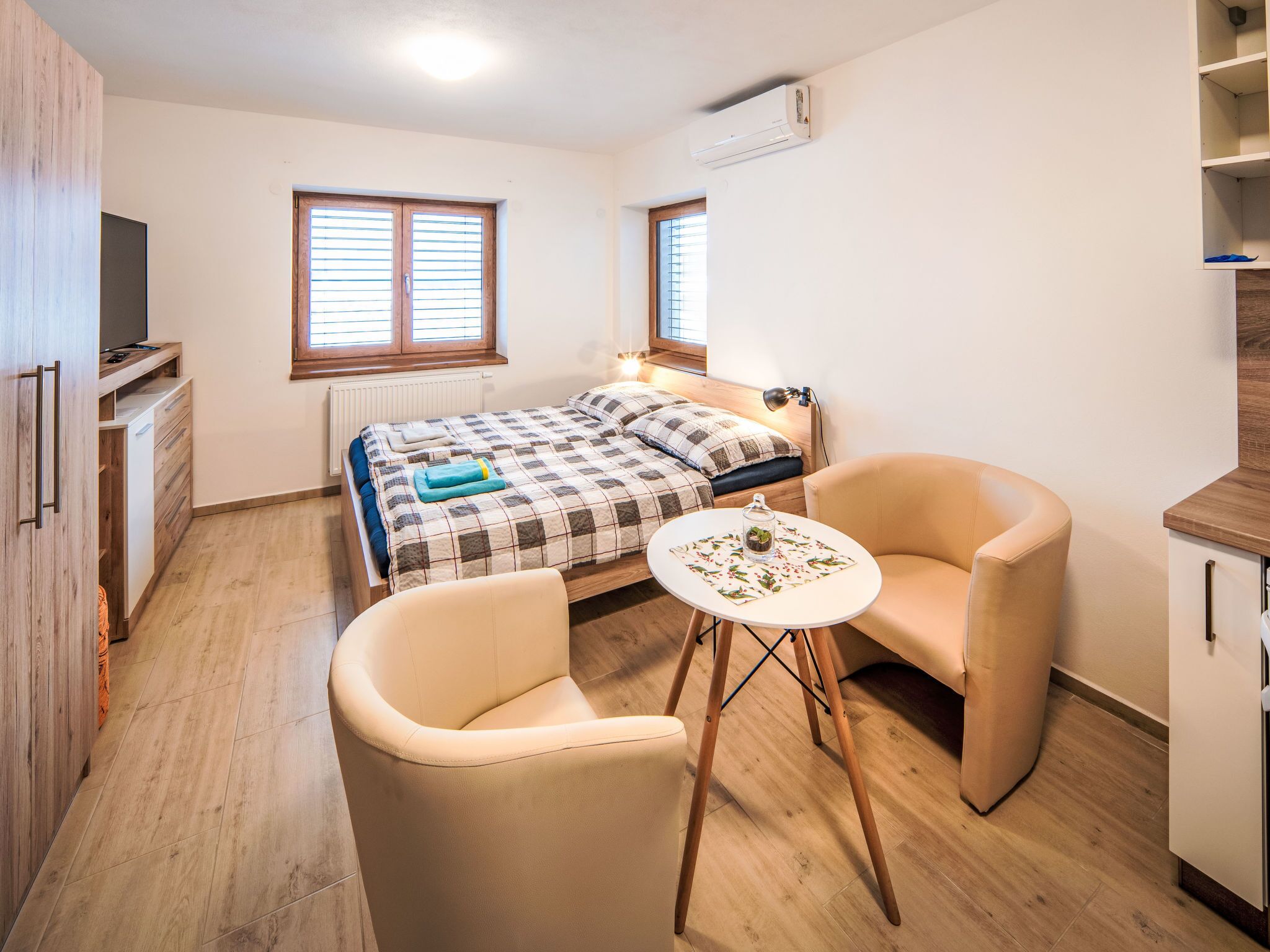Ein Schlafzimmer mit einem Bett, zwei Stühlen, einem kleinen Tisch, einem Fernseher und einem Fenster.