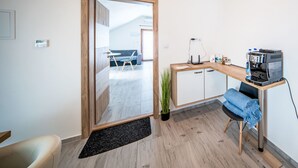 A modern room with a wooden desk, a coffee machine, a plant, and a view of the outdoors.