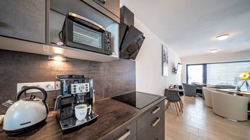 Une cuisine moderne équipée d’un four à micro-ondes encastré, d’une machine à café, d’une bouilloire et d’une tasse à café posée sur le plan de travail.