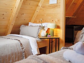 Ein gemütliches Schlafzimmer im Dachgeschoss mit Holzwänden, einem Bett mit Rüschenbettwäsche, einem Nachttisch mit Lampe und einer kleinen Pflanze.