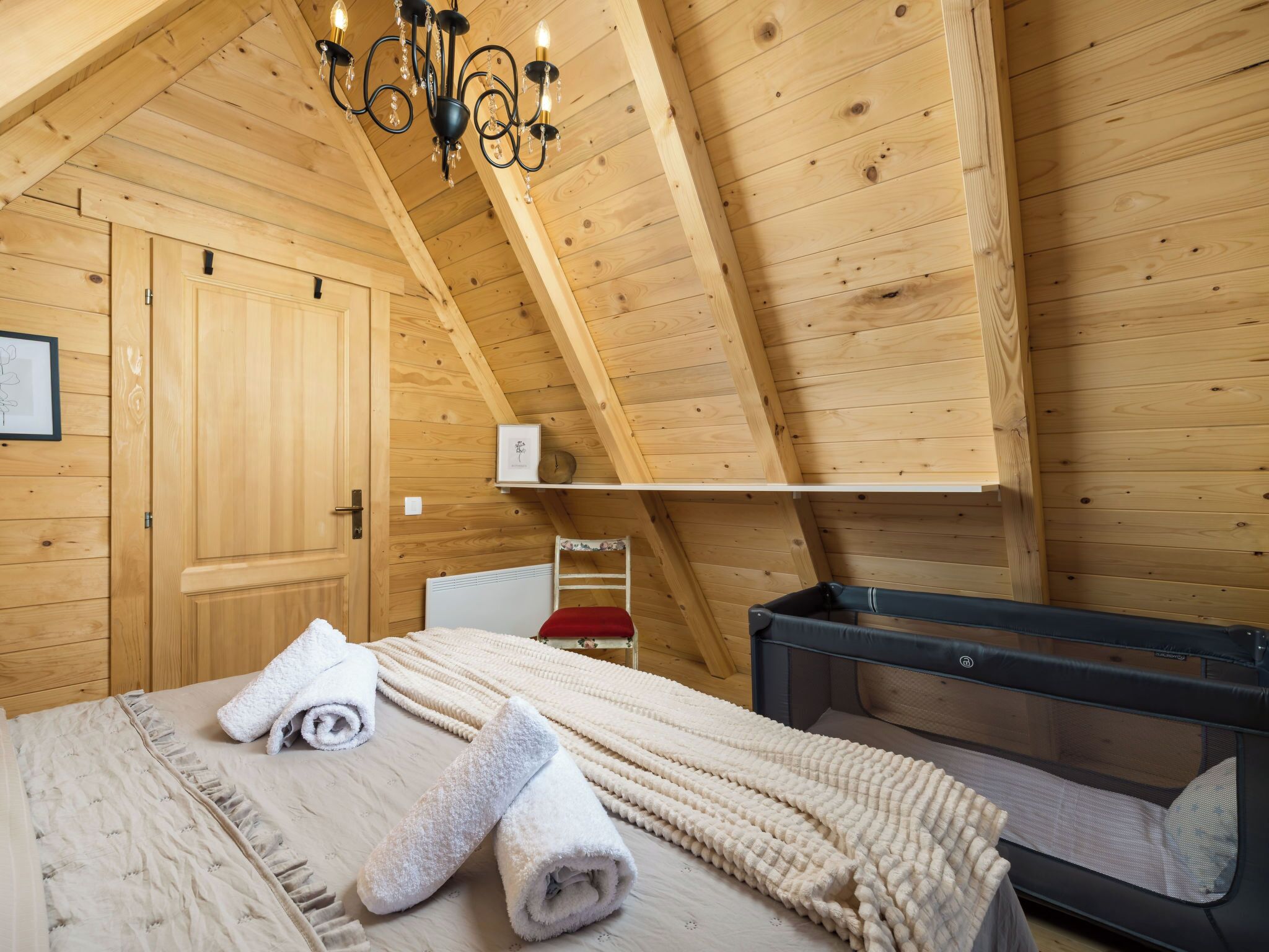 Une pièce en bois avec un lit, une commode, un radiateur et un lustre.