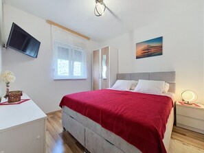 Et soveværelse med en seng, et fjernsyn, et vindue, et billede og et natbord med en lampe.