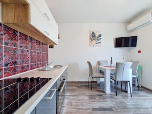 Eine moderne Küche mit roter Küchenrückwand, ein Essbereich mit Tisch und Stühlen sowie ein an der Wand befestigter Fernseher.
