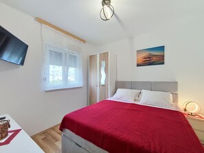 Un dormitorio con una cama, un televisor, una ventana, una puerta y un cuadro en la pared.