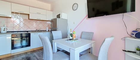 Eine moderne Küche mit weißen Schränken, einem eingebauten Ofen und einem Essbereich mit weißem Tisch und grauen Stühlen.