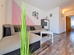 Un salon moderne avec un canapé d’angle, une petite table blanche et une grande plante verte.