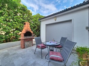 Een terras met een bakoven, een tafel met stoelen en een garagepoort.