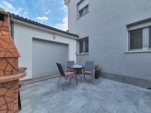 A patio with a table and chairs, a closed garage door, and a building with windows. - Apartment Vigi by Interhome (Pag/Povljana)