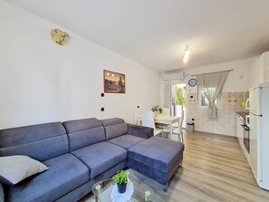 A modern living room with a grey sectional sofa, a glass coffee table with a plant, and a dining area with a white table and chairs. - Apartment Vigi by Interhome (Pag/Povljana)