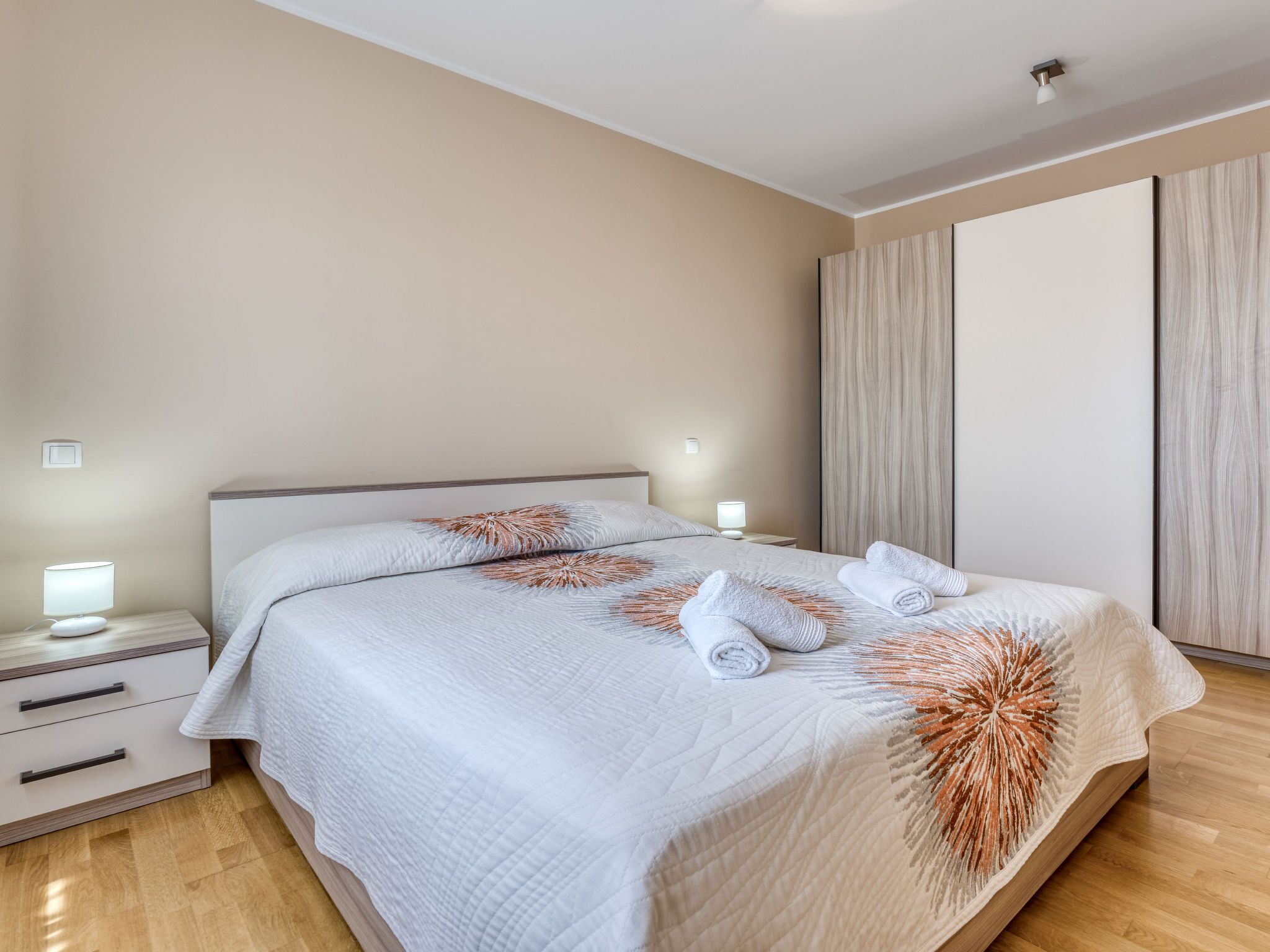 Una camera da letto moderna con un letto grande, comodini con lampade, un armadio e un pavimento in legno.