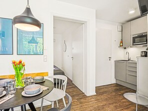 Eine moderne Küche mit Mikrowelle, Spüle und Schränken. Ein Essbereich mit Tisch für zwei Personen, einer Vase mit Tulpen und einem Stuhl.
