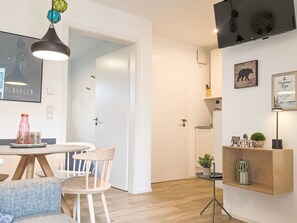 A modern living room with a round dining table, white chairs, a hanging light fixture, and a mounted television. - Dümmer Koje 761 (Seenähe) by Interhome (Lembruch)