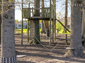 Eine Spielgerüstkonstruktion mit einer Holzplattform, Seilen und einem Netzbereich.
