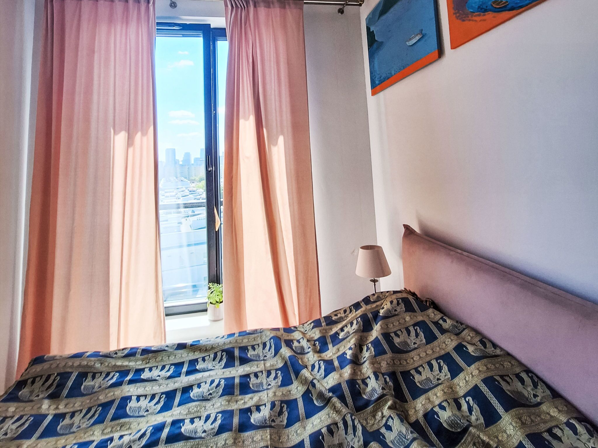 Ein Zimmer mit Bett, Vorhängen, einem Fenster mit Stadtblick und einer Lampe.