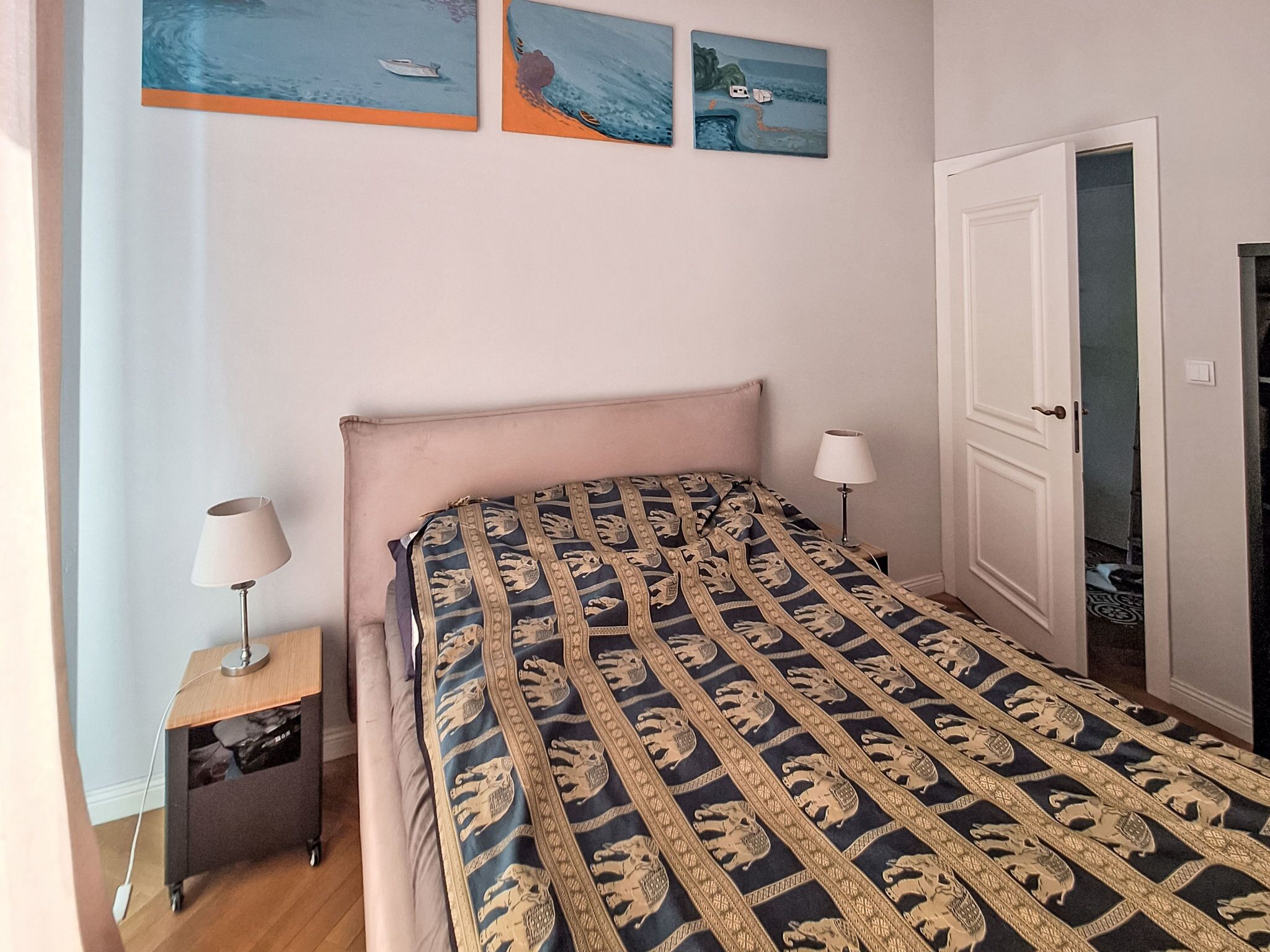 A bedroom with a bed, bedside tables, a door, and wall art.