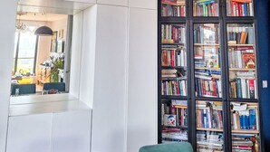 A modern living room with a large bookshelf, a dining area with a table and chairs, and a view through a window. - Dzielna by Interhome (Warsaw)