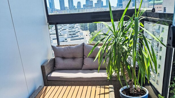 A balcony with a cushioned seating area, a potted plant, and a city skyline view. - Dzielna by Interhome (Warsaw)