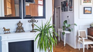 A living room with a fireplace, a potted plant, a white chair, and a wall with artwork. - Dzielna by Interhome (Warsaw)