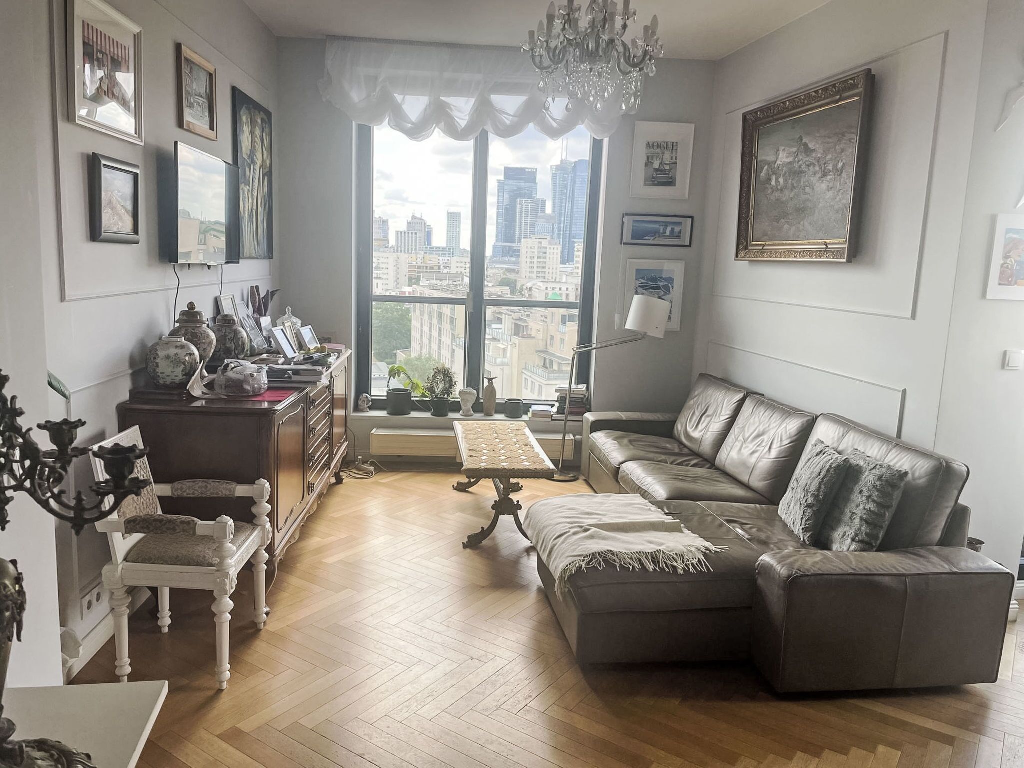 Un salon comprenant un canapé, une table, une chaise, une bibliothèque et une fenêtre donnant sur la ville.