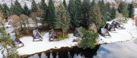 A lakeside cabin area with several cabins, a dock, and a snowy landscape.