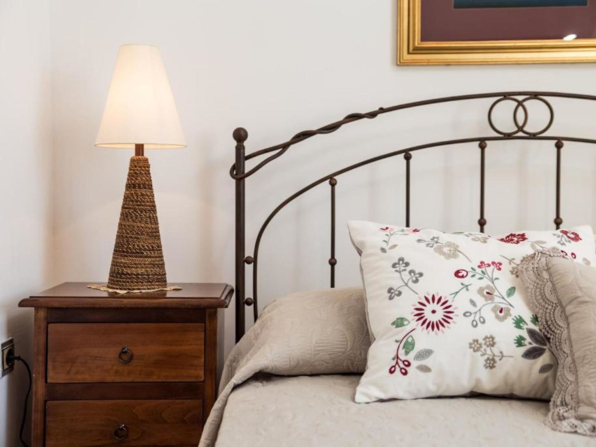 A bed with a floral pillow, a bedside lamp, and a wooden nightstand.