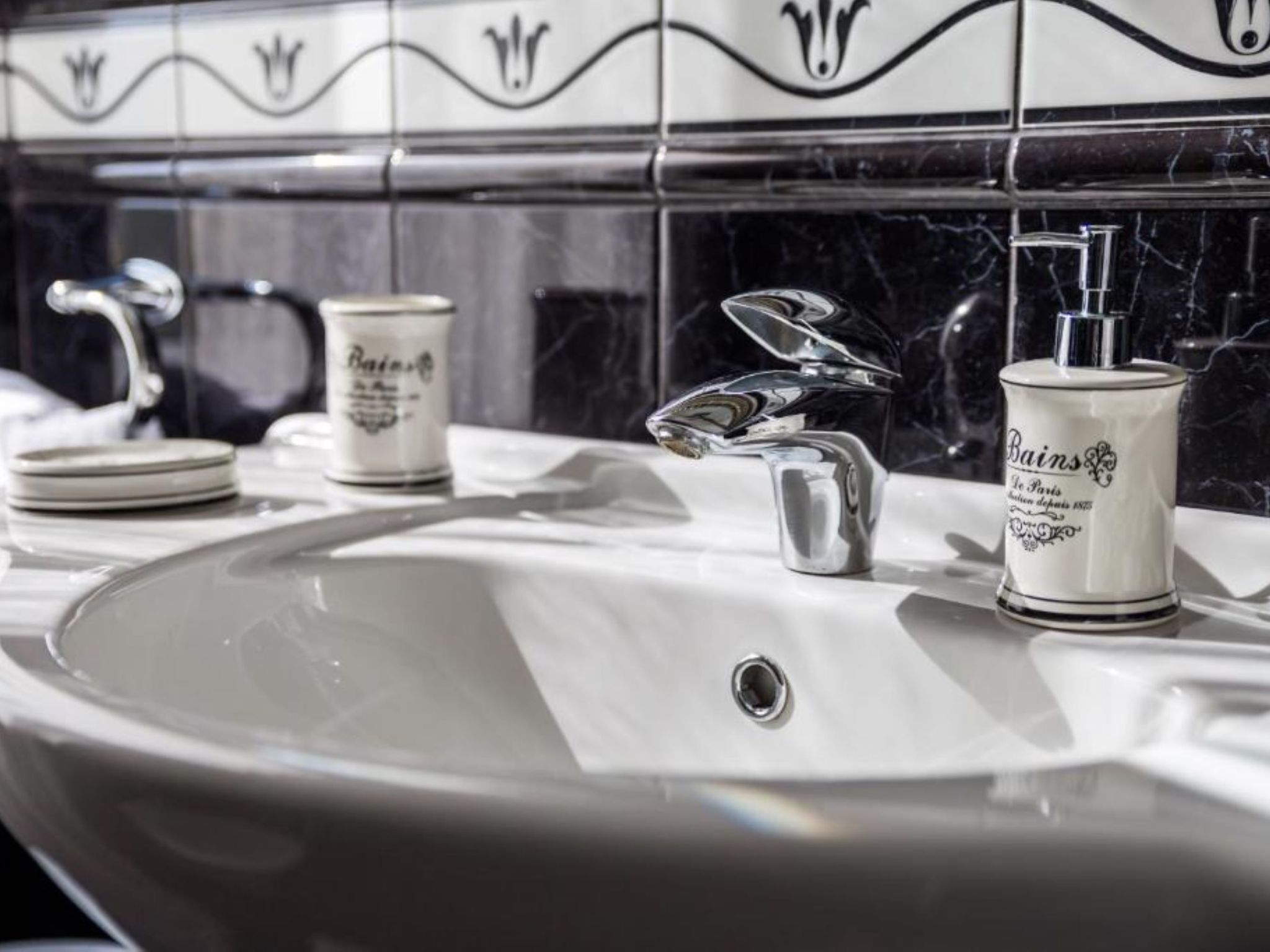 Un lavabo de salle de bain avec un robinet chromé, une bouteille de savon Bains de Paris et un petit récipient.