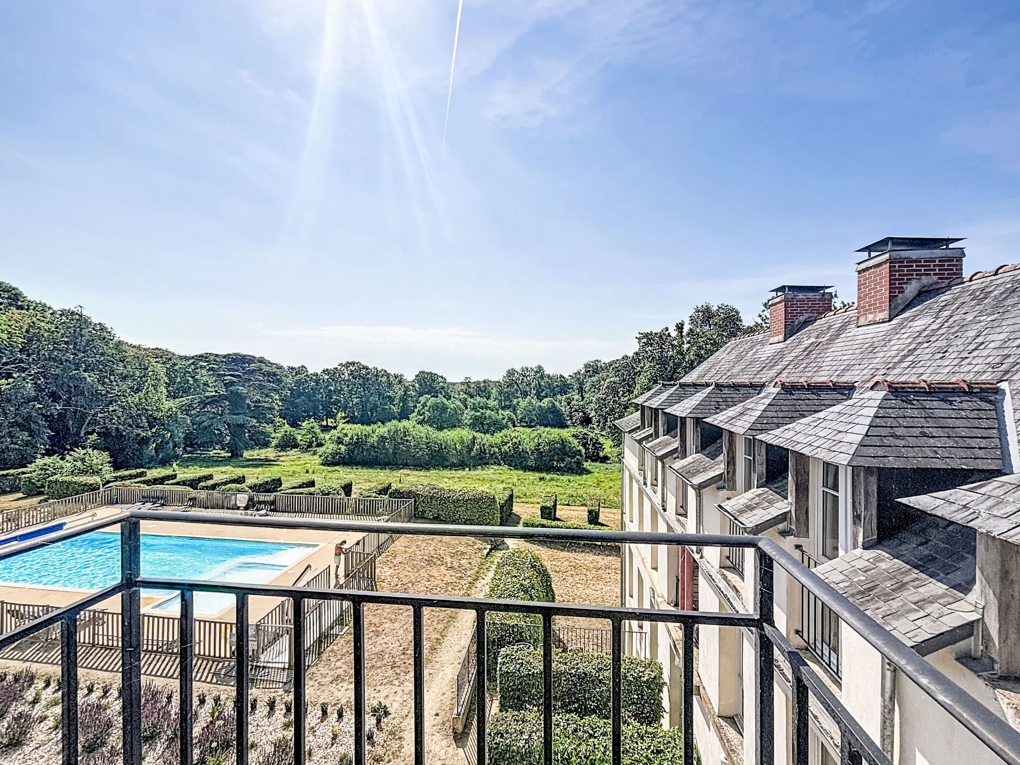 A residential property with a swimming pool, a well-maintained garden, and a view of a forested area.