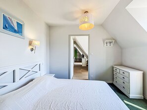 A bedroom with a bed, dresser, wall art, and a hallway leading to a staircase. - Le Château de Kergonano by Interhome (Baden)