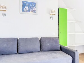 En grå soffa med kuddar, en inramad målning som föreställer ett havsskepp, två vägglampor och en grön dörr.