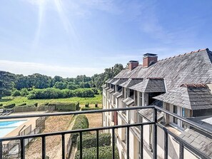Un edifici de diverses plantes amb un balcó, una piscina i vista a un paisatge verd.