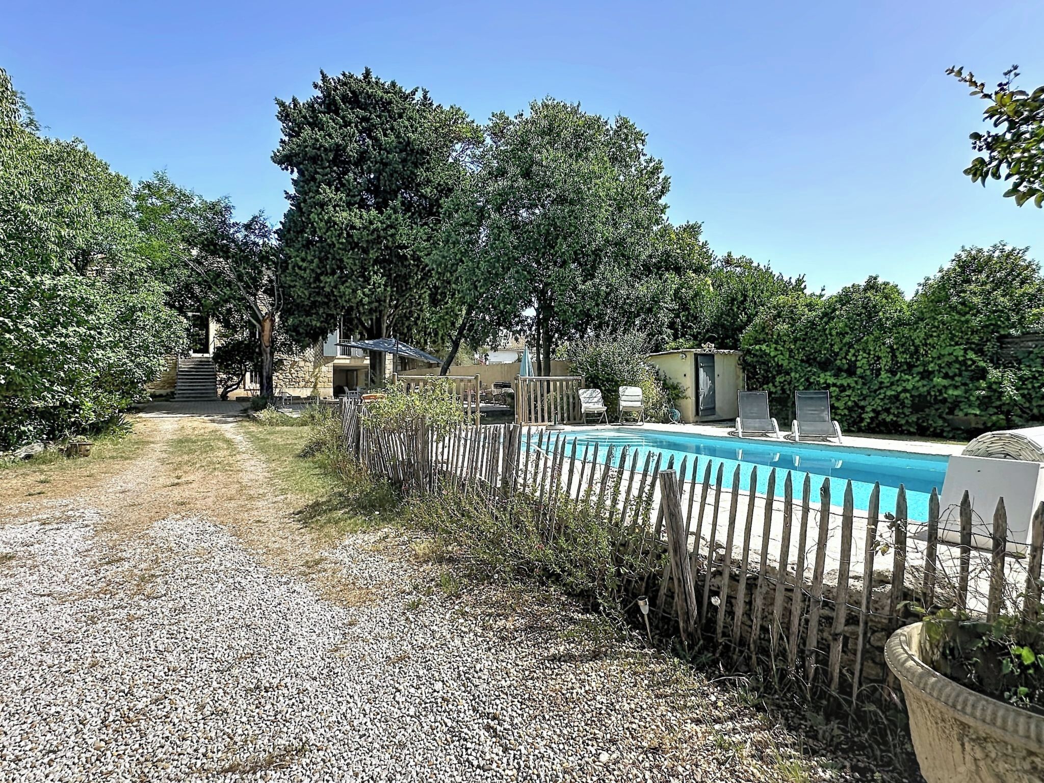 Un jardin avec une piscine, une clôture en bois et un chemin de gravier menant à une maison.