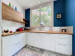 A modern kitchen with white cabinets, a wooden countertop, and a window with a view of pink flowers. - Villa Piscine - Aigues-Vives by Interhome (Aigues-Vives)