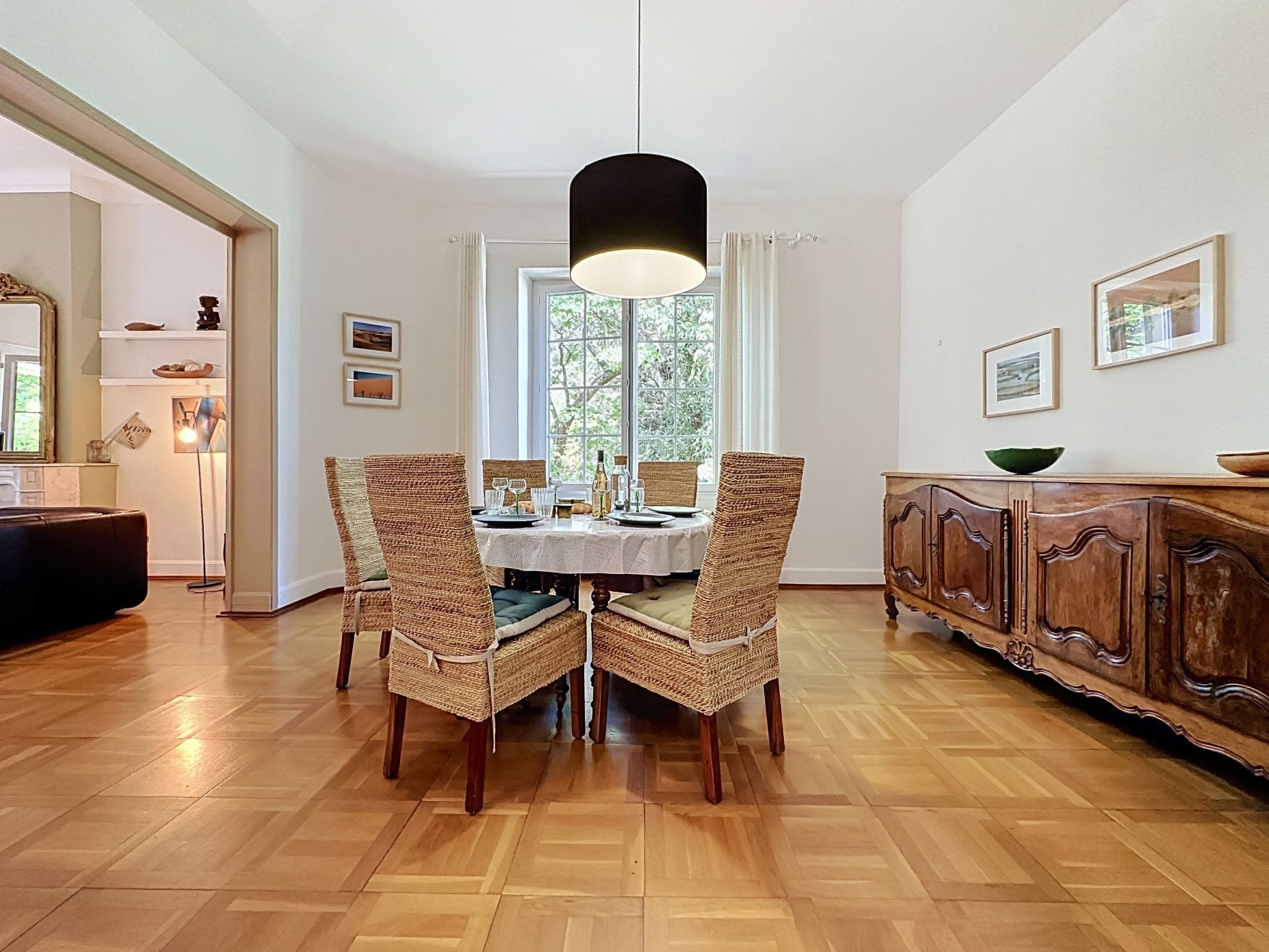 A dining area with a table set for four, surrounded by wicker chairs, a wooden cabinet, and a hanging light fixture.