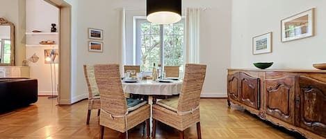 Comedor con una mesa dispuesta para cuatro personas, sillas de mimbre, un mueble de madera y una lámpara colgante.