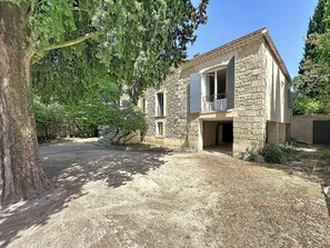A stone building with a balcony, a paved driveway, and surrounding trees. - Villa Piscine - Aigues-Vives by Interhome (Aigues-Vives)