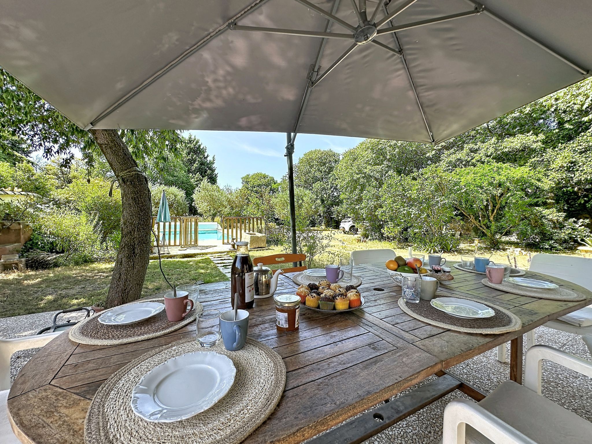 An outdoor dining area with a table set for four, surrounded by greenery and a pool in the background.