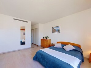 A bedroom with a bed, a wardrobe, a mirror, a picture on the wall, and a hallway leading to another room. - Lydia Playa by Interhome (Le Barcarès)
