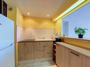 A compact kitchen with wooden cabinets, a white refrigerator, and a window with a view. - Lydia Playa by Interhome (Le Barcarès)