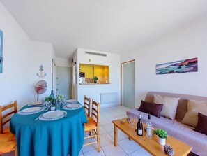 A dining area with a table set for four, a sofa, a coffee table with bottles, and a kitchen in the background. - Lydia Playa by Interhome (Le Barcarès)