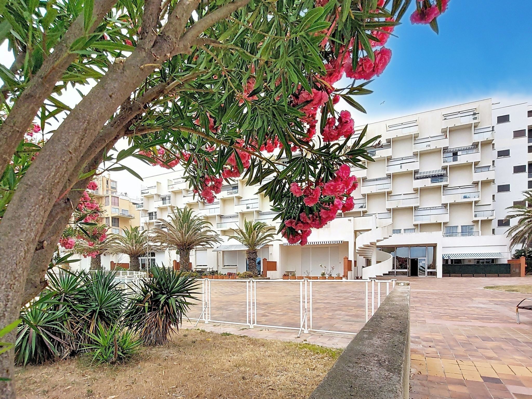 A residential building with balconies, a paved courtyard, and surrounding greenery.