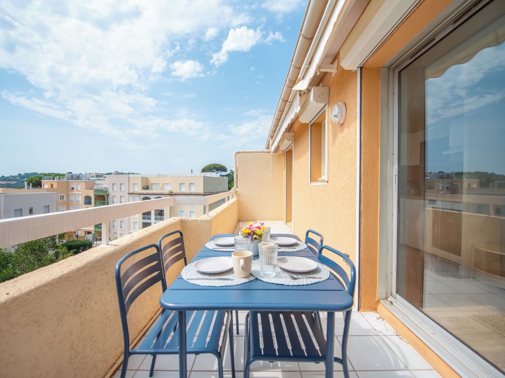 A balcony with a table set for four, chairs, a vase with flowers, and a view of the cityscape.
