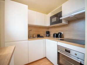A compact kitchen with white cabinetry, a wooden countertop, a built-in microwave, a coffee maker, and an oven. - Santa Barbara by Interhome (Cavalaire)