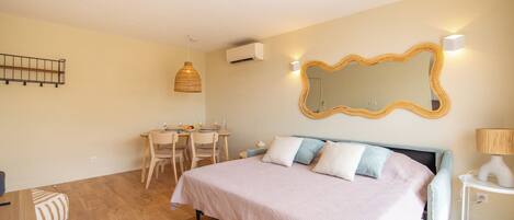 A bedroom with a bed, bedside table, lamp, and a dining area with chairs and a table.
